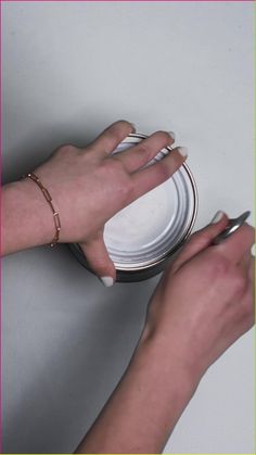 two hands with manicures are using scissors to paint a white plate on the wall