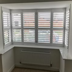 an empty room with white shuttered windows and radiator in the corner,