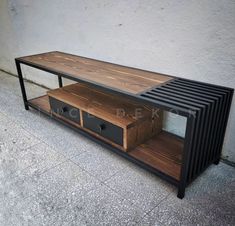 a wooden and metal tv stand on the ground next to a white wall with two drawers