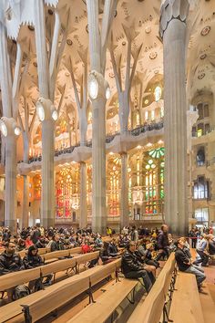 many people are sitting on benches in the middle of a large room with high ceilings