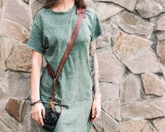 a woman standing in front of a stone wall with a camera strap around her neck