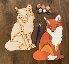 two cutouts of foxes sitting next to each other on a wooden table with eggs and paintbrushes