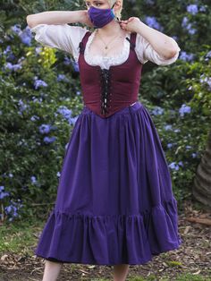 a woman wearing a purple dress and mask with her hands on her face while standing in front of blue flowers