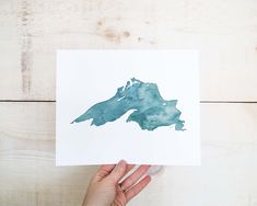 a person holding up a piece of paper with watercolor paint on it that looks like the shape of a map