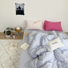 an unmade bed with blue sheets and pink pillows on the bottom, next to a white wall