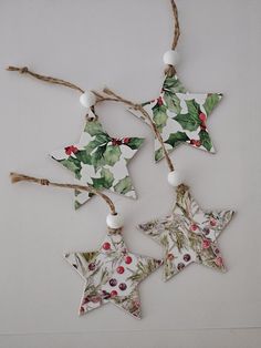 three christmas decorations hanging from twine with holly leaves and berries on them, one star shaped ornament