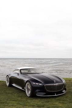 a black car parked on top of a grass covered field next to the ocean and water