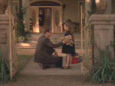 a man kneeling down next to a woman in front of a house