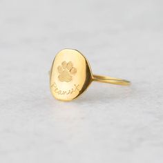 a gold ring with a dog's paw and name engraved on the front, sitting on a white surface