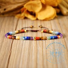 a multicolored beaded bracelet sitting on top of a wooden table next to flowers