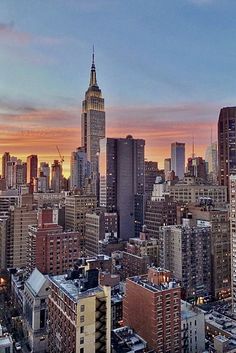 the sun is setting over new york city, with skyscrapers in the foreground