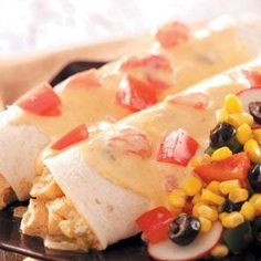 an enchilada with corn, black olives, tomatoes and cheese on it