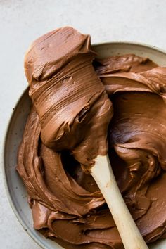 a bowl filled with chocolate frosting and a wooden spoon