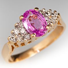 This sweet ring is centered with an oval cut pink sapphire, weighing 1.00 carat, in a four-prong setting. The shoulders are each bead set with six (6) round brilliant cut diamonds. The ring measures 6.9mm at the top, rises 6.3mm above the finger, tapering to 2.0mm wide and 0.7mm thick at the base of the shank. The ring currently fits a size 4.75. Luxury Pink Gold Sapphire Ring As Gift, Classic Pink Sapphire Diamond Ring With Center Stone, Classic Pink Round Cut Sapphire Ring, Formal Oval Pink Sapphire Ring, Pink Oval Diamond Ring With Accent Stones, Oval Pink Sapphire Diamond Ring With Accents, Oval Pink Diamond Ring With Accent Stones, Classic Pink Sapphire Round Cut Ring, Classic Pink Diamond Ring With Center Stone