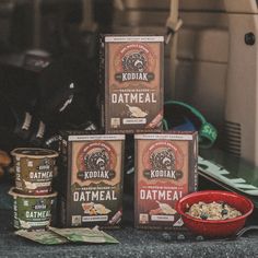 three boxes of oatmeal sitting on top of a counter next to a red bowl