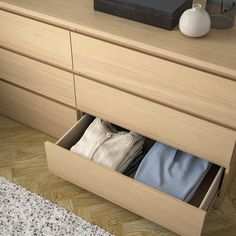 an open drawer with clothes in it on a wooden floor next to a white vase