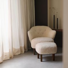 a chair and foot stool in front of a window with curtains on the outside wall