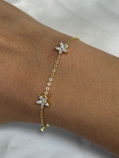 Elevate your style with our exquisite flower bracelet decorated with crystals. This delicate gold chain bracelet showcases intricate flower-shaped decorations, each embellished with dazzling clear or white gemstones, resembling the brilliance of diamonds. The design exudes simplicity and elegance, making it a perfect accessory for any occasion. Add a touch of sophistication to your ensemble with this stunning piece.   Specs: Material: Solid Sterling Silver, 14k Gold Plated Stones: Round white cu Flower-shaped Cubic Zirconia Bracelets As Gift, Gold Flower-shaped Bracelets For Party, Flower Shaped Cubic Zirconia Bracelets As Gift, Flower-shaped Cubic Zirconia Bracelets For Gifts, Flower-shaped Cubic Zirconia Bracelet For Gifting, Elegant Crystal Bracelet With Flower Charm, Gold Flower Bracelets With Cubic Zirconia, Gold Cubic Zirconia Flower Bracelets, Gold Jewelry With Sparkling Flower Stones