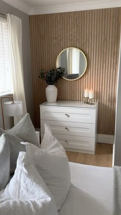 a white bed sitting next to a dresser with a mirror on it's side