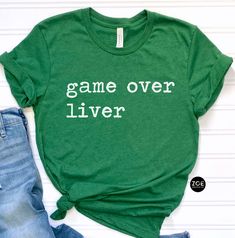 a green shirt that says game over liver on it next to jeans and a pair of shoes