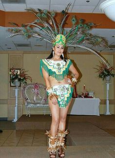 a woman in a green and gold costume with feathers on her head standing next to a table