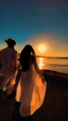 a man and woman walking along the beach at sunset, with the sun in the background