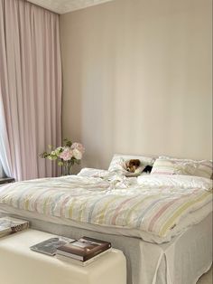 a bedroom with a large bed and pink drapes on the windowsill, along with a white footstool