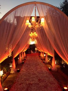 an outdoor wedding with white drapes and candles on the aisle, surrounded by flowers