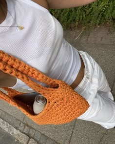 a woman is holding an orange crocheted purse with a soda can in it