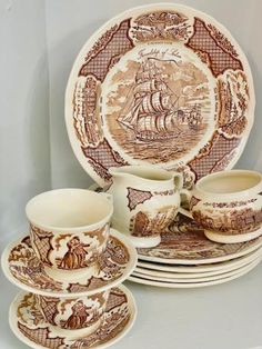 a set of brown and white china with an image of a ship on the plate