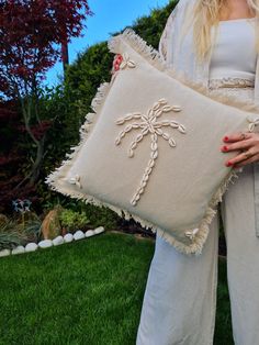 a woman holding a pillow with a cross on it in her hands and wearing white pants