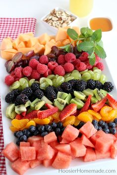 a white platter filled with fruit and veggies next to a glass of orange juice