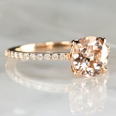 an engagement ring with a fancy cushion cut morganite surrounded by small white diamonds on a marble surface