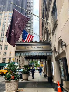 people walking down the sidewalk in front of a building with an american flag on it