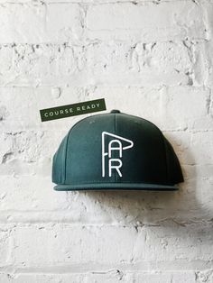 a green hat hanging on the side of a white brick wall with a sign reading course ready