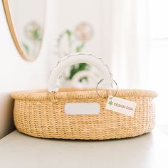 a wicker basket with a label on it sitting on a table next to a mirror