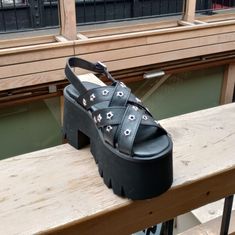 The Demonia Ashes-12 In Black Has A 3" Platform With Slight 3.75" Heel And Criss-Crossing Front Straps With Star Grommet Hardware, As Well As A Plain Black Adjustable Back Strap. #Demonia #Demoniaashes #Demoniaashes12 #Ashes12 #Platformsandal Silver Platform Sandals For Spring, Spring Silver Platform Sandals, Summer Party Sandals With Silver Studs, Spring Open Toe Sandals With Silver Studs, Spring High Heels With Silver Studs, Summer Open Toe Sandals With Silver Studs, Silver Sandals With Studded Rubber Outsoles And Round Toe, Spring Silver Studded High Heels, Black Open Toe Sandals With Silver Studs