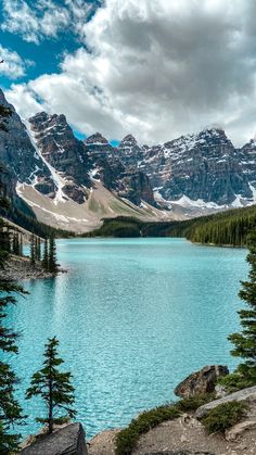 a lake surrounded by mountains and trees under a cloudy sky