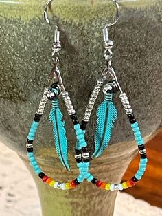 Beaded hoop earrings with a turquoise native flame worked into the pattern at the bottom and a turquoise feather in the middle. Beaded Earrings With Feathers, Western Earring, Seed Bead Jewelry Tutorials, Native Decor, Beading Designs, Beaded Items, Native Beading, Western Crafts, Beaded Jewelry Earrings