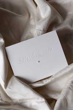 the bridesmaid card is laying on top of white satin