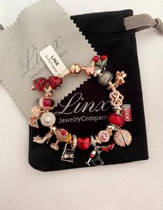 the charm bracelet is in red and gold with charms on it, along with a tag that says love jewelry company