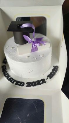 a white cake with a purple ribbon and a graduation cap on top in a box