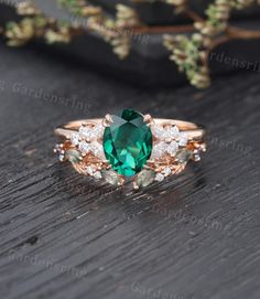 an oval green stone surrounded by white diamonds on top of a wooden table with greenery in the background