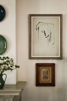 a painting hangs on the wall next to a vase with flowers in it and two framed pictures