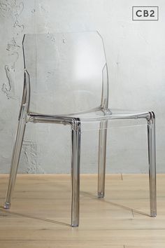 a clear plastic chair sitting on top of a wooden floor next to a white wall