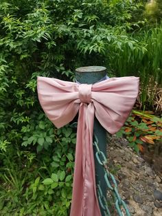 a pink bow tied on top of a metal pole in front of some bushes and trees