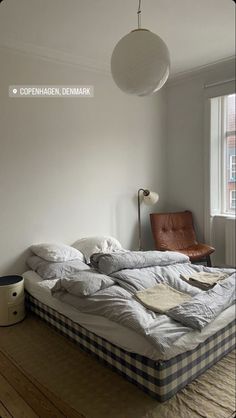 an unmade bed sitting on top of a hard wood floor next to a window