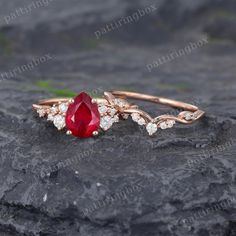 a close up of a ring with a red stone and diamonds on it, sitting on top of a rock