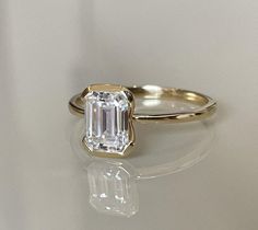 an emerald - cut diamond ring sits on a white surface