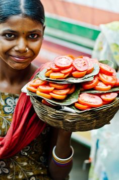 a woman holding a basket full of sliced tomatoes